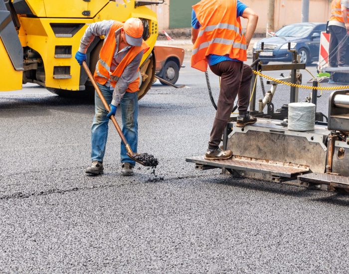 A team of road workers repairing a section of the road with the help of an asphalt paver and a road roller